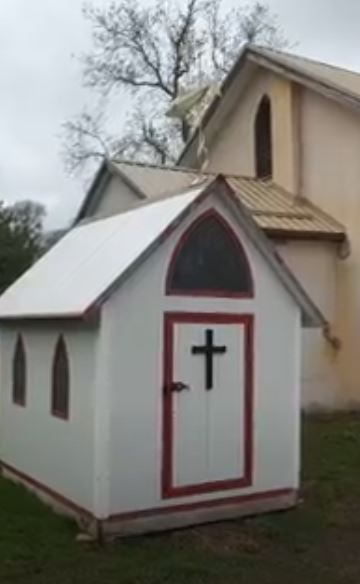 White ice fish hut chapel with red trim and black cross on door
