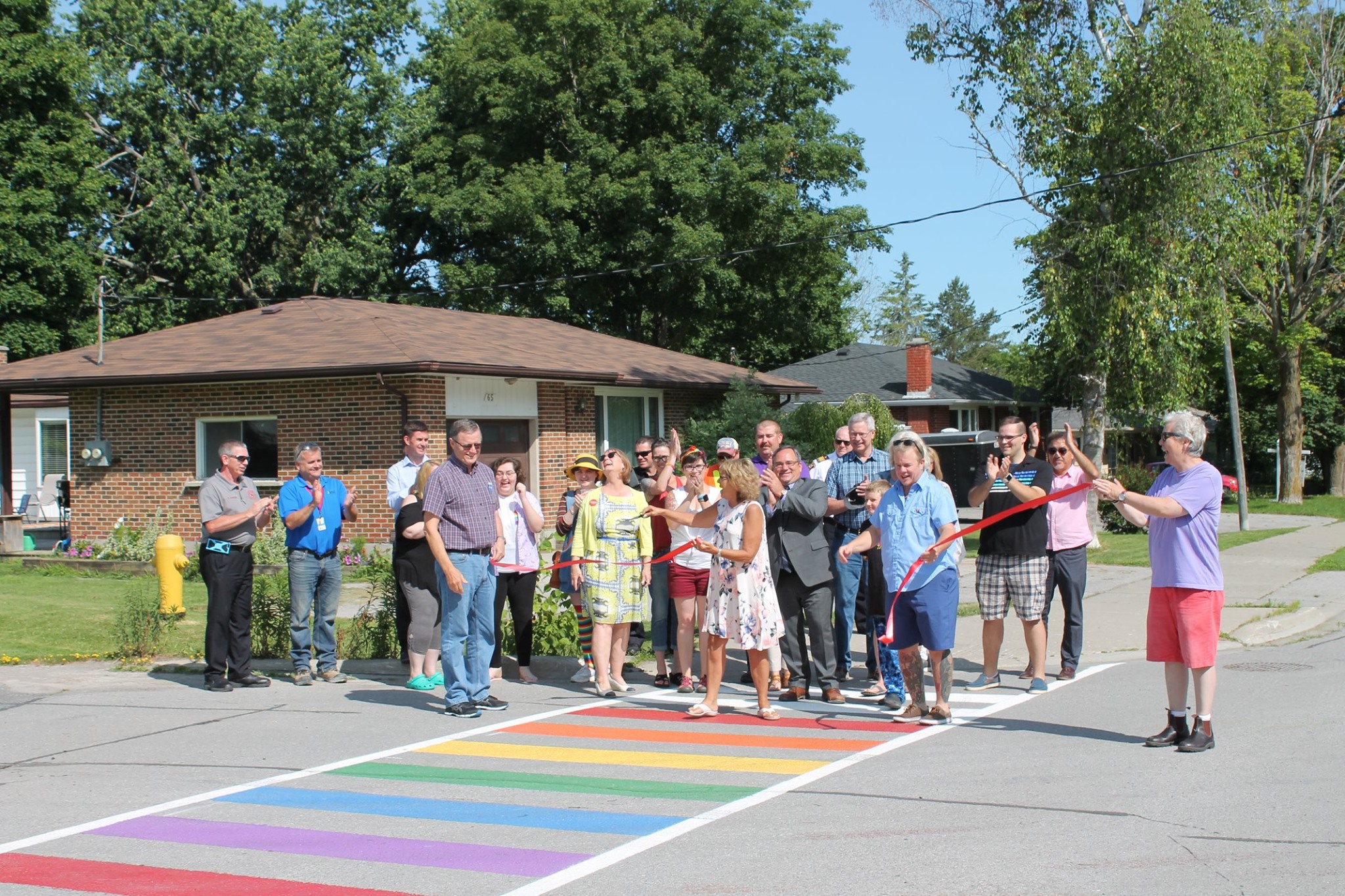 Group smiling and clapping as the ribbon is cut at the rainbow crosswalk